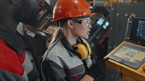 Caucasian female plant worker explaining African American male colleague how to operate CNC machine using special digital equipment with sensor screen