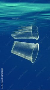 Vertical video, Close-up of plastic cup slowly floating underwater, slow motion.Transparent disposable acrylic glass floats under water reflecting on its surface during calm