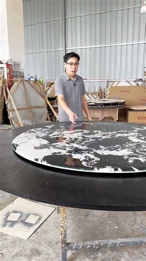 An extendable round rotating dining table with a black stone/marble pattern top and dark wood