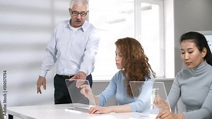 Medium tracking shot of senior Caucasian computer education teacher explaining college students how to use transparent touchscreen devices with tapping and expanding hand gestures. Suitable for AR, VR