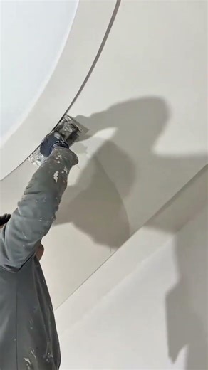 Spreading white plaster on curved ceiling using manual trowel to create smooth surface decoration