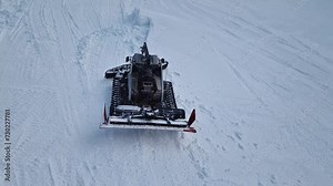 Aerial view of a snowcat working as leveling the snowdrifts on the slopes at Bansko ski resort in Bulgaria. Snow grooming machine in the mountains