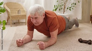 Happy smiling mature senior man doing exercises of gymnastics at home. Concept of healthy lifestyle, fitness, recreation, well being. Elderly male exercising training, stretching. Old man working out