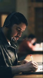 young Latino works studies in the library in the evening. searches for information in a laptop on the Internet and makes notes in a notebook. use of artificial intelligence. Vertical video footage