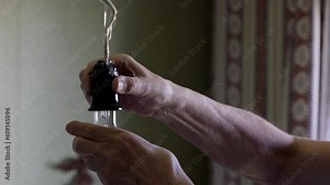 An Elderly Man's Male Hands Screw An Old Light Bulb Into The Chandelier Socket On The Kitchen Ceiling And The Bulb Lights Up. 4k. 60 FPS.