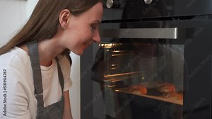 Woman looks into the oven through the glass at the food being cooked.