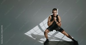 Sporty man in activewear doing physical exercise on yoga mat in studio with white background. Athletic male has workout and doing side lunge exercise. Warm up concept