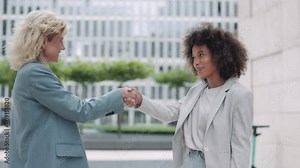 Multicultural business ladies shaking hands outdoors