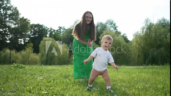 Mother helps toddler first steps. Family bonding nature as toddler takes first steps. Toddler first steps with family support. Family milestone in nature. Happy family moment with toddler first steps