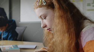 Close-up side shot of geeky teenage Caucasian girl with bright red hair sitting in programming class, busy with writing computer code on laptop, typing on keyboard and peering at screen