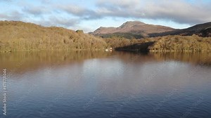 Aerial drone footage reversing over Loch Lomond near the West Highland Way to reveal Ben Lomond Mountain (Munro) and the surrounding landscape in autumn in Loch Lomond and the Trossachs national park.