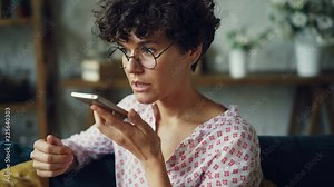 Smiling young woman is dialing telephone number then talking in loudspeaker mode holding smartphone in hand. Modern technology and communication concept.