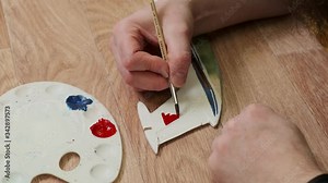 master hand draws with red color on wooden tail unit of passenger jetliner model at table at Sunday school closeup slow motion