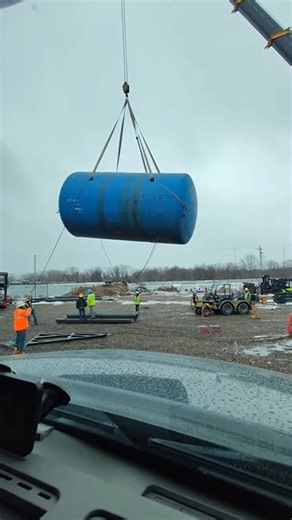 Rigging Failure Drops Massive Industrial Tank Gary, Indiana — May 15, 2025 A routine industrial lift turned into a terrifying close call Tuesday afternoon when a massive blue storage tank slipped from its rigging and crashed to the ground. Workers at the riverside construction site watched in horror as the multi-ton vessel tilted and then plummeted, sending a massive plume of dirt and debris into the air. Footage captured from a nearby vehicle shows the crane hoisting the tank high above the gro