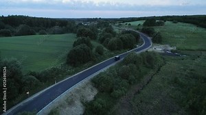 In this cinematic aerial drone camera footage you can see blue jeep car driving on asphalt road in countryside landscape. Action in remote location early in the morning before the sunrise at dusk.