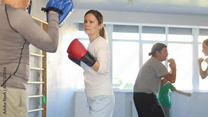 Woman works out strength and speed of boxing punch mitts with help of male partner in boxing paws. Man performs role of target and mannequins during training strike technique