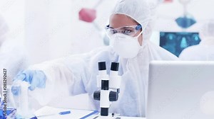 Chemical scientist using modern microscope in research laboratory. Scientist analysing a sample of blue solution on microscope.