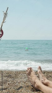 Fishing in the sea, a homemade fishing rod, a bell swinging in the wind, men's feet on the sand. Vertical. Social Media