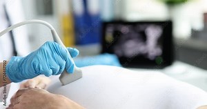 Doctor conducts ultrasound examination of abdomen of young pregnant woman in modern clinic. Pregnant woman getting sonogram from gynecologist