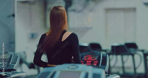 Woman with long hair runs on a treadmill in the gym. Exercise in the gym. View from the back.