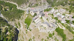 Fortified Castle Of Fort Queyras At The Hilltop And The Village Of Chateau-Ville-Vieille In Hautes-Alpes, France. aerial orbiting