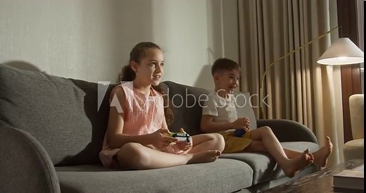 Children enjoy multimedia games. Cute little girl and boy smiles, kids are playing video games on the tv, actively plays computer games sitting on sofa in living room. Children playing computer games.