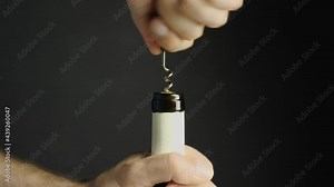 Opening a bottle of wine. Men's hands twist the corkscrew into the cork, and then take it out of the bottle. Close-up. Black background