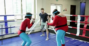 Women in red leggings are boxing with a trainer. Fat overweight woman hits the coach in the boxing ring.