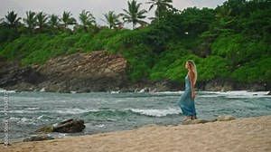 Elegant woman in azure dress strolls serene tropical beach. Relaxed stroll, tranquil sea waves splash, caress sandy beach, soothing nature scene for mental wellness, vacation vibe.