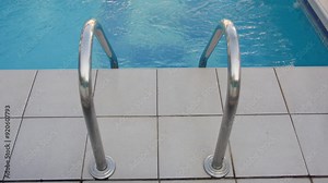 Stainless steel ladder leading into a clear blue swimming pool. Focuses on the steps and railings against the pool water