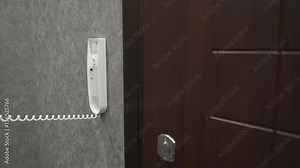 Person holding handset of intercom system installed on a wall in the apartment answering a call