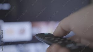 Man watches smart TV and uses black remote control. Person controls TV using a modern remote control choosing channels from a smart tv. Closeup 4k cinematic shot. Shallow depth of field