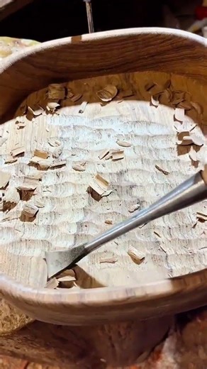 carving a large wooden bowl using a sharp metal gouge tool to create intricate textured patterns