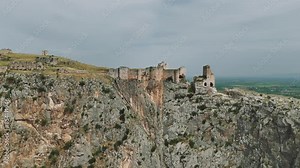 A drone flies over the ruins of Anavarza Castle, perched atop a towering mountain in Adana, Turkey. Witness the imposing cliffs and ancient structures