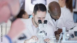 Research scientists make a discovery in the lab, looking into microscope and discussing analysis.