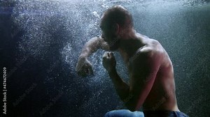 Male athlete boxer underwater, training punches and diving under the surface of a dark pool
