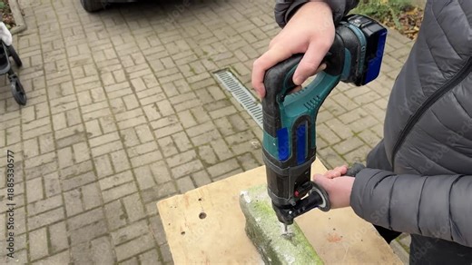 A person drills into a flat concrete block with a cordless hammer drill on a bench outdoors, mid close.