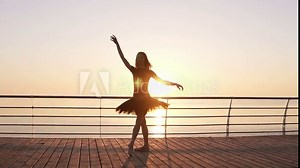 Dancing ballerina in black ballet tutu and pointe on seafront above ocean or sea. Morning bosk. Young attractive woman practicing, making vertical twine, lunge forward in the dance