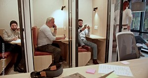 Business associates are immersed in work within compact, modern office booth settings, showcasing concentration and teamwork in their tasks.