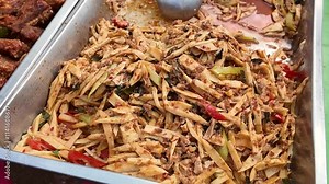 Spicy Bamboo Shoot Stir-fry: A vibrant dish of bamboo shoots stir-fried with chilies and other spices, creating a tantalizing aroma and texture. The dish is presented in a metal container.