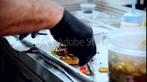 4K Cinematic food cooking footage of a chef preparing and making a delicious homemade burger in a restaurant kitchen in slow motion putting the toppings on top of the smashed burger