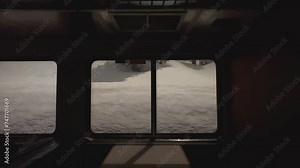 Train window view of snowbanks rolling by in a hilly, snowy forest. The interior shows booth seating, with seats on either side of a table for passengers to eat dinner. The Sierra Nevadas are outside.