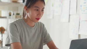 Close-up Young Asia girl IT development programmer typing on keyboard coding programming fixing data code on laptop computer screen follow code plan in tablet and paperwork on table at house office.