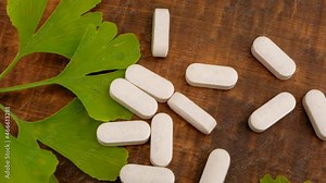 Ginkgo biloba pills . homeopathic white pills with ginkgo extract and ginkgo leaves on wooden background . Alternative medicine and homeopathy.4k footage