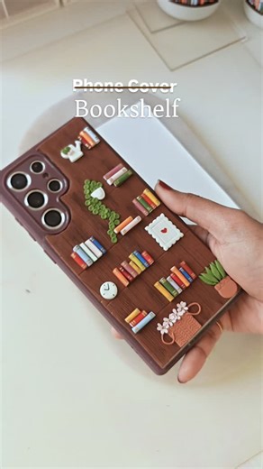 The Bookish Pandora ✦ Studio on Instagram: "Who says your bookshelf has to stay at home? When we carry our phones everywhere, why not carry what feels like home on it? This phone cover is handmade using polymer clay - a tiny bookshelf with books, plants, and quiet details for people who live between pages. For readers who don’t just read books… they belong to them 🤍 bookish phone case, bookshelf phone cover, polymer clay phone case, handmade phone cover, book lover aesthetic, miniature bookshel