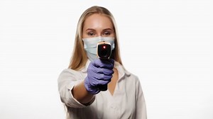Médecin ou infirmière pointant le thermomètre du capteur sur la caméra portant un masque de protection en robe blanche d'hôpital médical. Jeune infirmière blonde vérifiant la température des patients ou des collègues de travail. 4k UHD