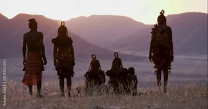 4K view of people from the Himba tribe in traditional dress, watching the sun setting on the mountains, Namib desert, Namibia