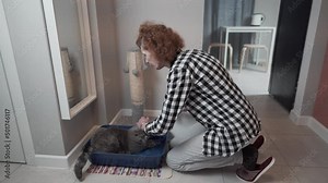 Senior woman assembles new cat litter box together with pet at home. Elderly female playing with cat sets hooded litter box for pet to go to toilet. Pet care, hygiene concept. Hooded cat litter pan.