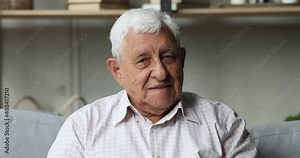 Head shot portrait single grey-haired senior 70s baby boomer generation man sit on sofa in living room smile look at camera. Medical insurance cover for older citizen, dental service clinic ad concept