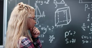 Caucasian small teen girl standing at blackboard in classroom, thinking and deciding math formulas and equations. Teenage smart schoolgirl studying mathematics at chalkboard. Algebra or geometry class
